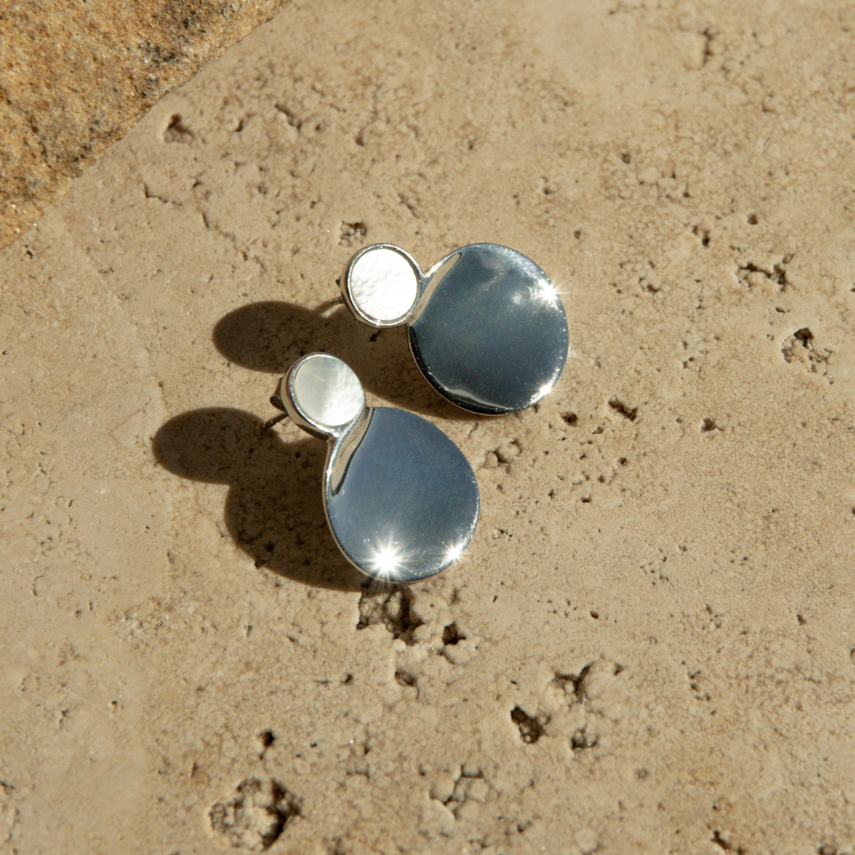 Silver earrings on a textured beige surface