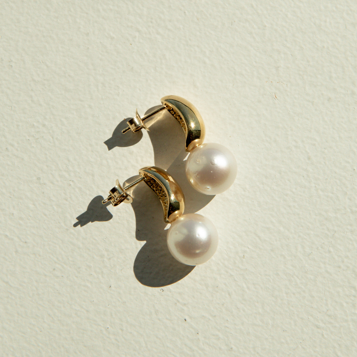 Gold hoop earrings with pearl accents on a light beige background