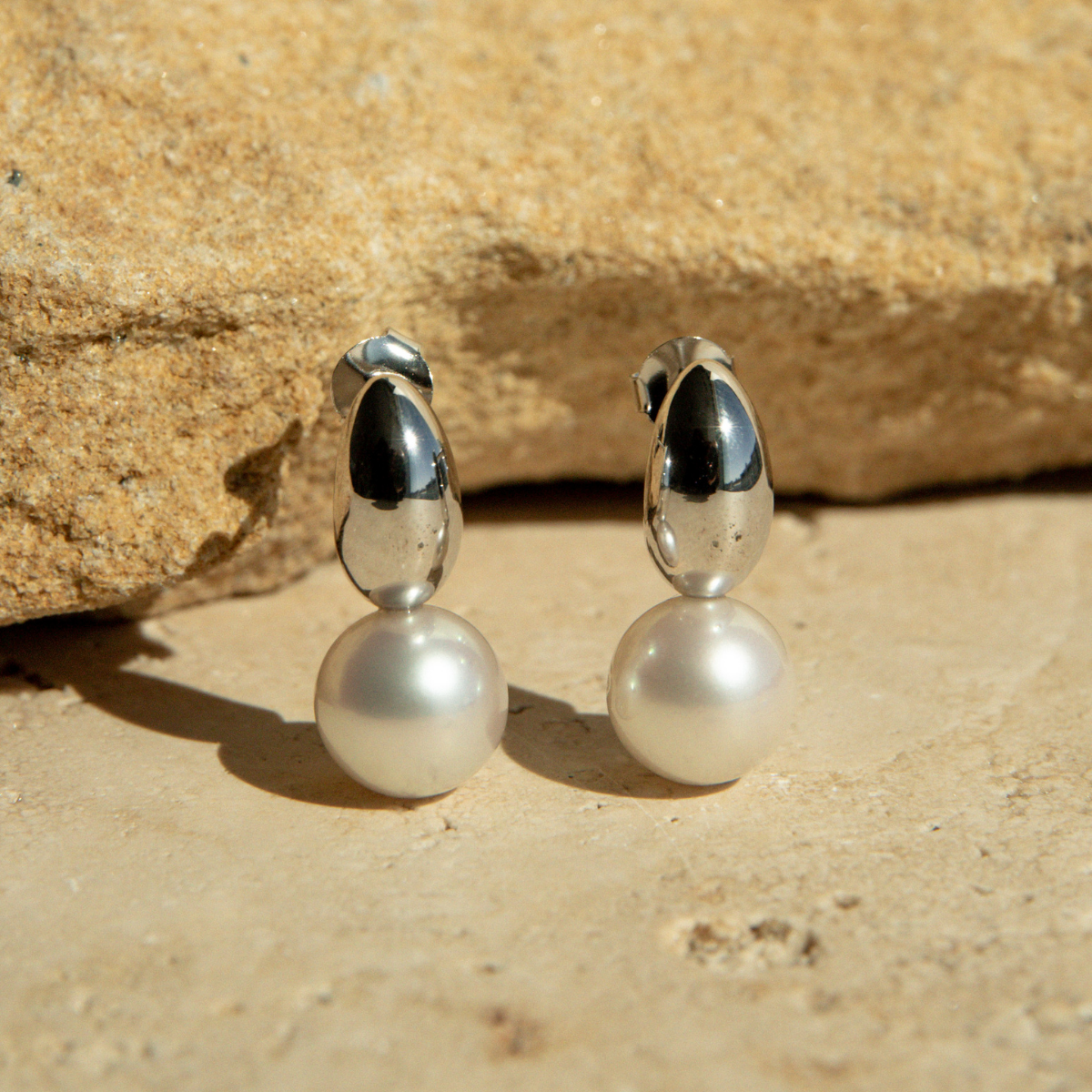 Pair of pearl earrings with silver tops on a stone surface
