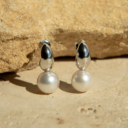 Pair of pearl earrings with silver tops on a stone surface