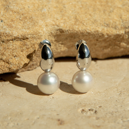 Pair of pearl earrings with silver tops on a stone surface