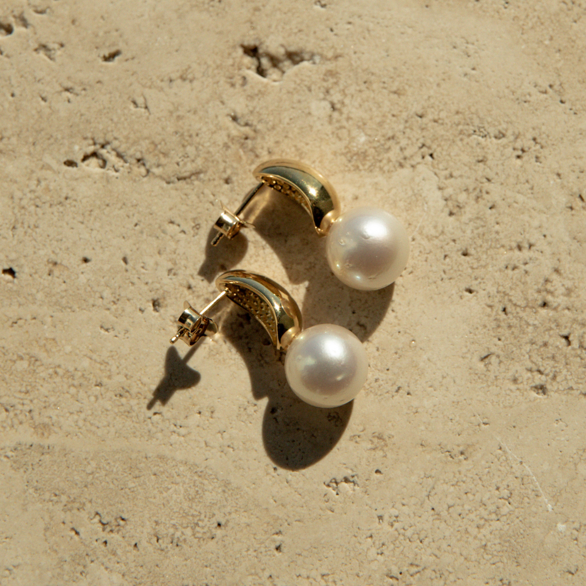 Pair of pearl earrings with gold posts on a beige stone surface