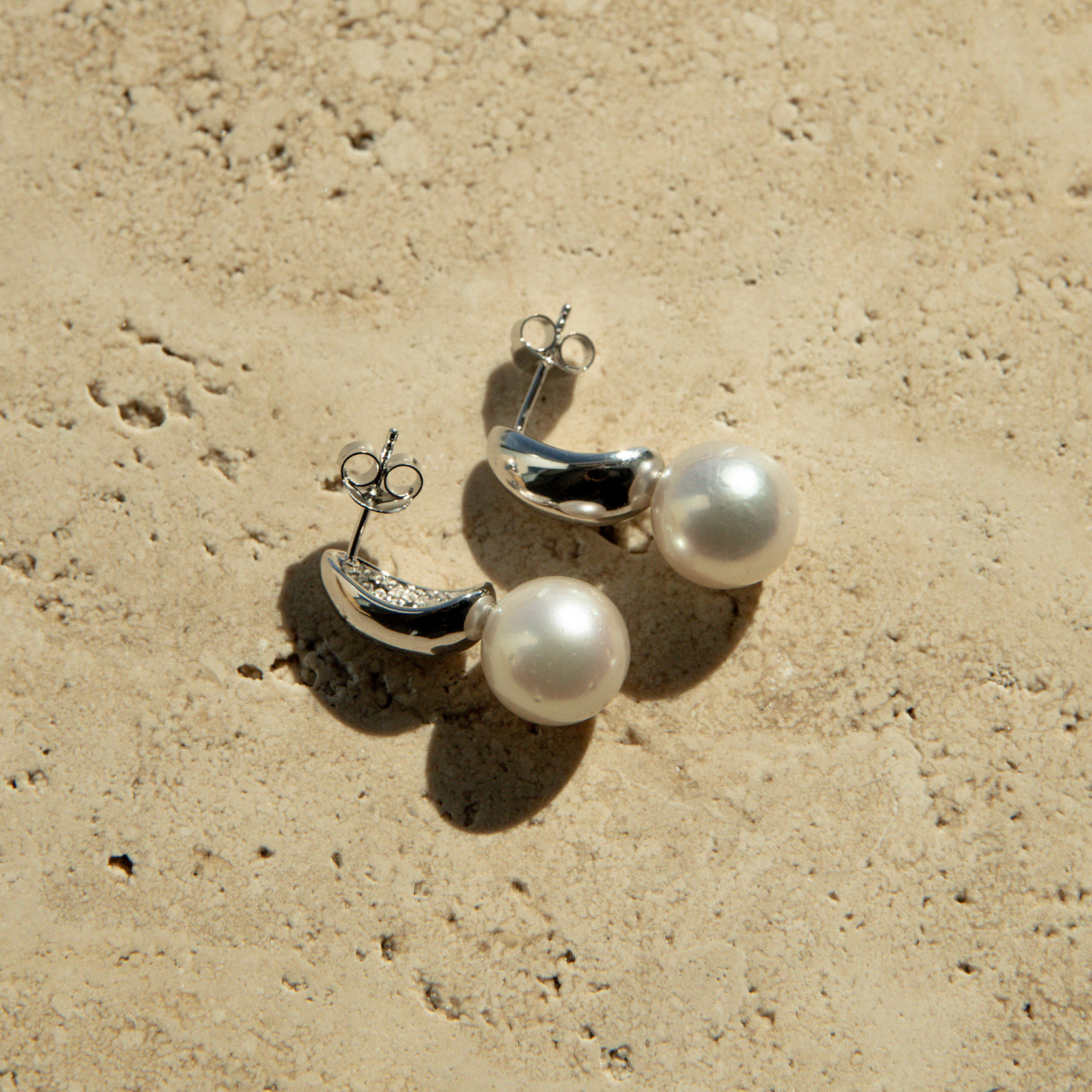 Pearl earrings on a textured beige surface
