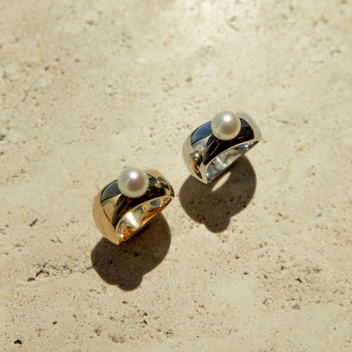 Gold and silver rings with pearls on a beige surface 