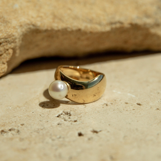 Gold ring with a pearl on a sandy surface