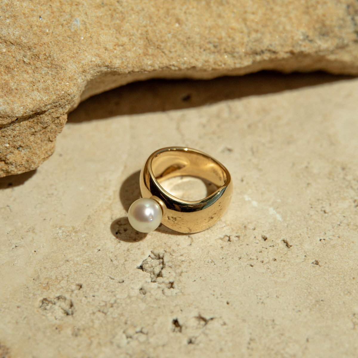 Gold ring with a pearl on a sandy surface