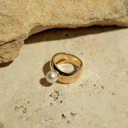 Gold ring with a pearl on a sandy surface