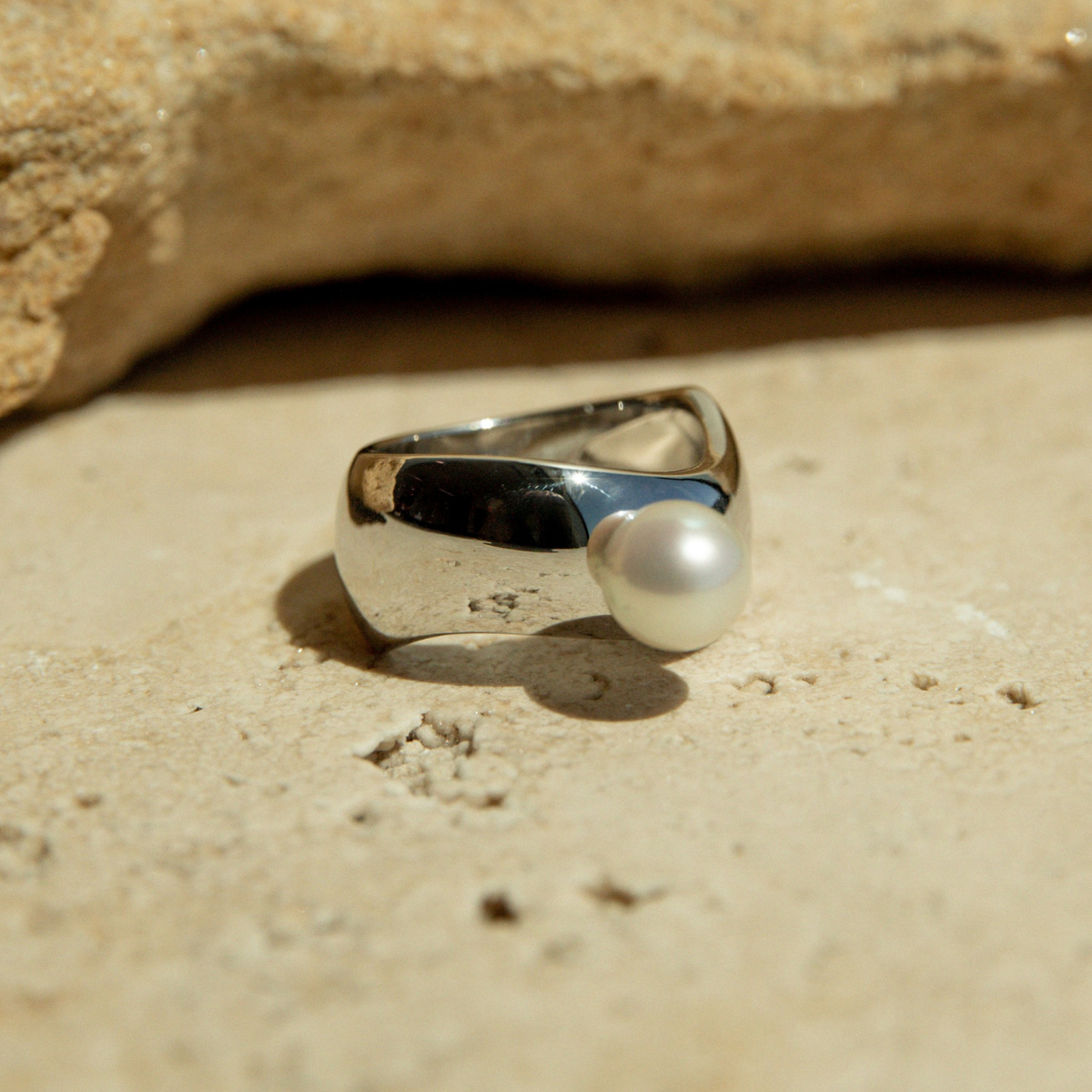 Silver ring with a pearl on a sandy surface