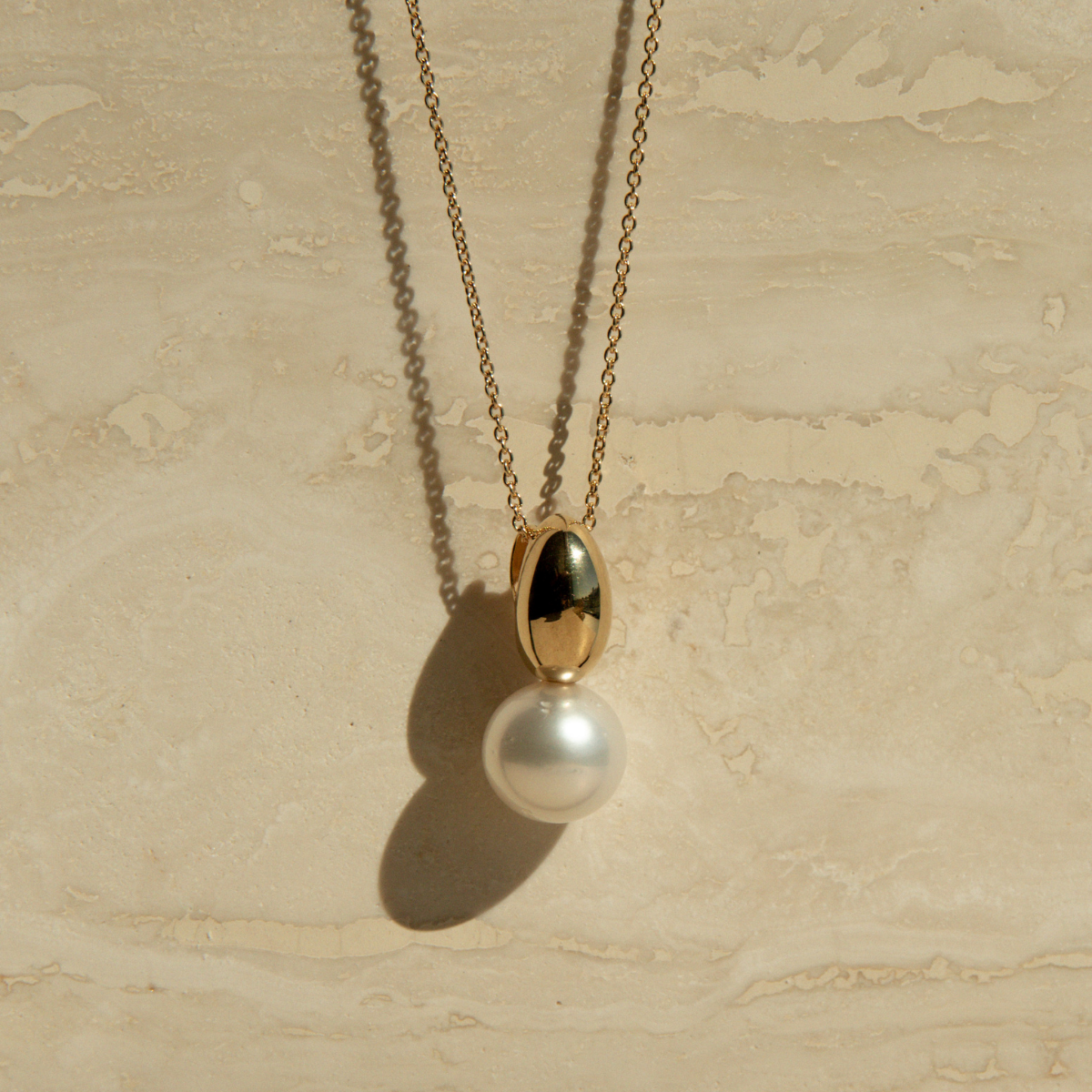Gold necklace with a pearl pendant on a beige stone surface