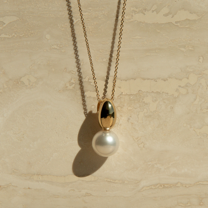 Gold necklace with a pearl pendant on a beige stone surface