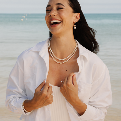 Woman on a beach wearing a pearl necklace and earrings.