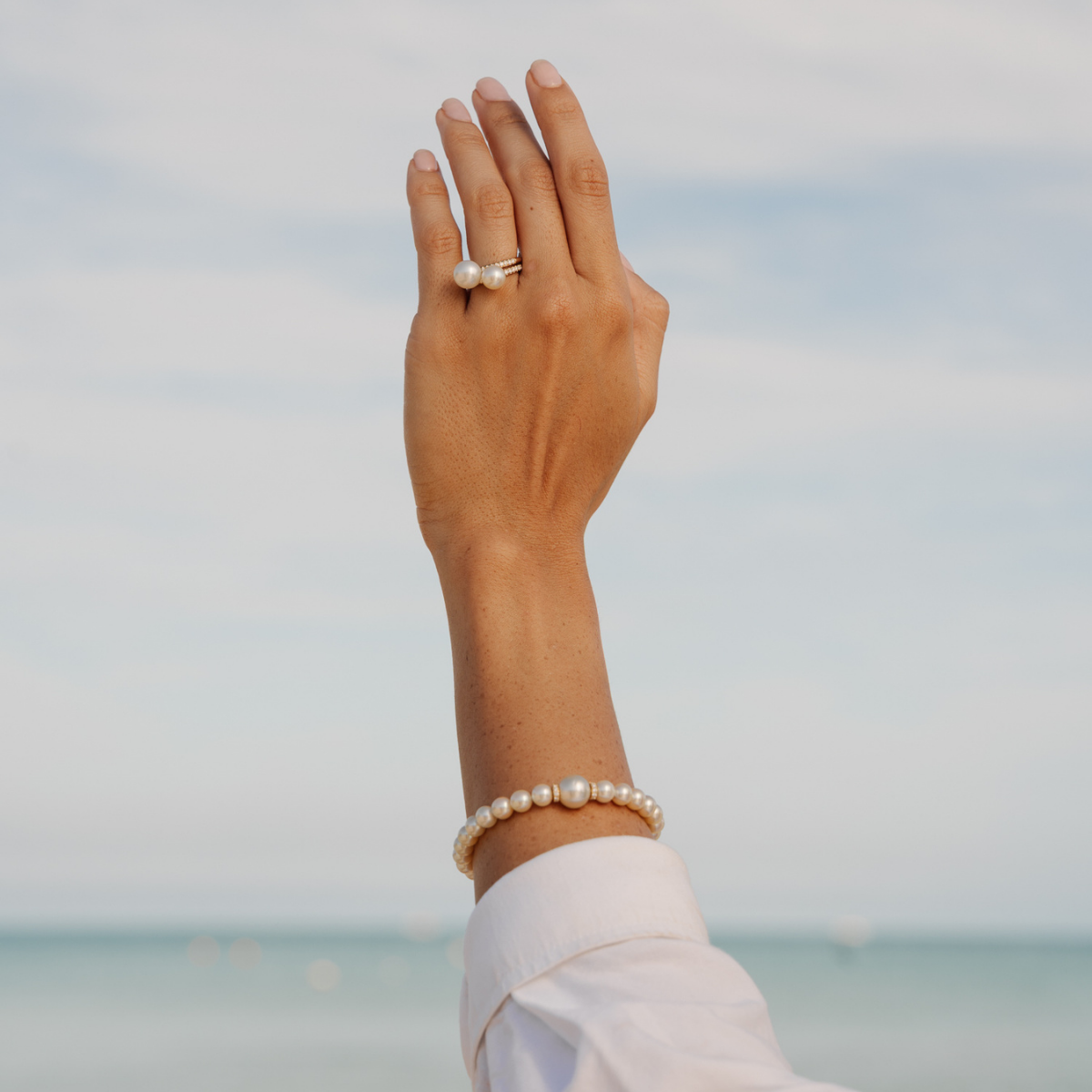 Hand wearing an eternal pearl ring and pearl bracelet with a blurred beach background