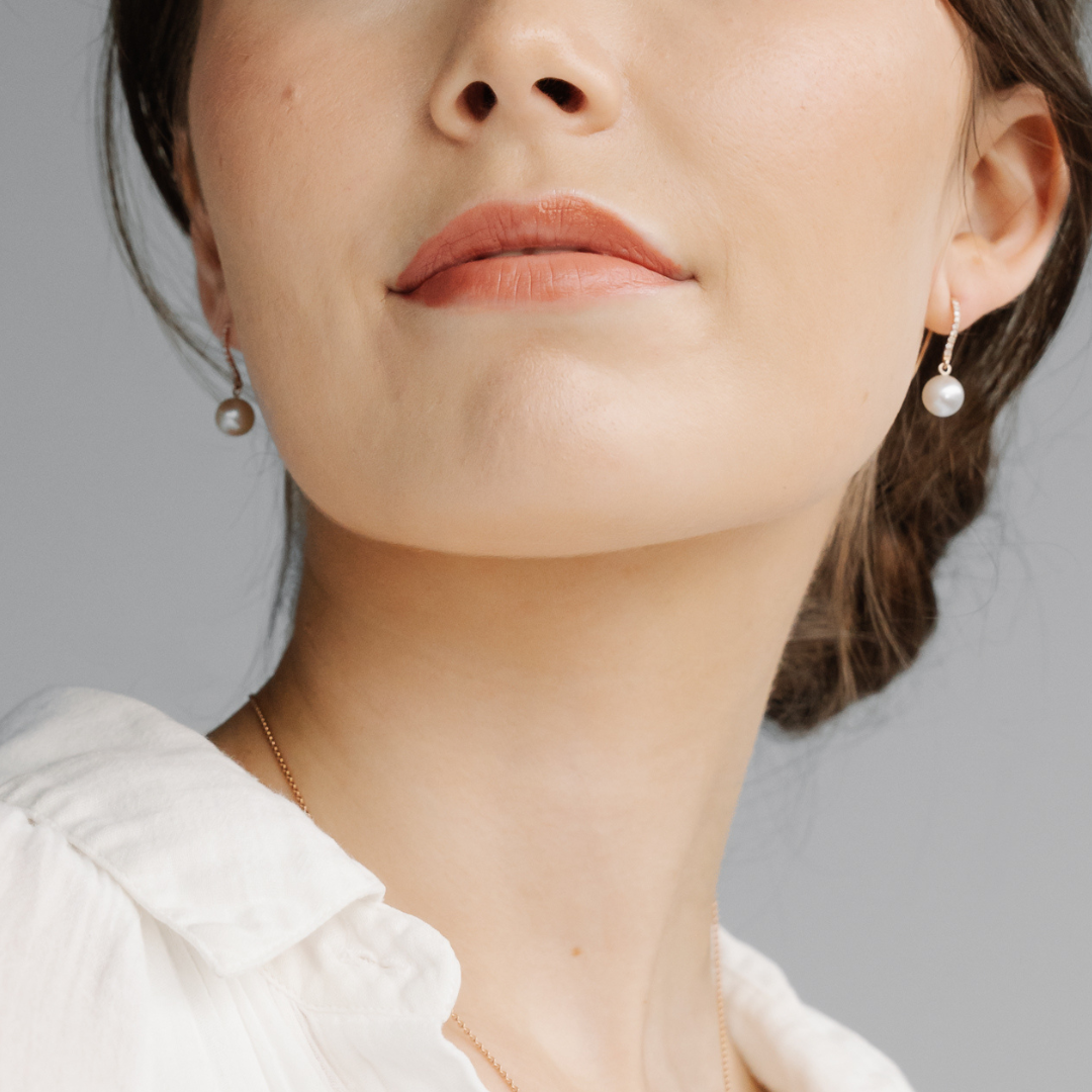 A woman wears her pair of stunning Australian Akoya pearl hook earrings set in gold, with a row of white diamonds. 