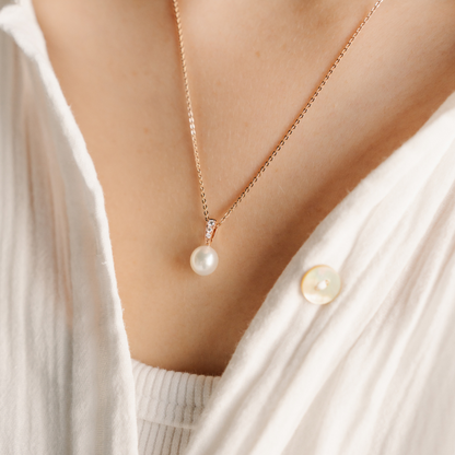 A woman wears her gorgeous Eternal Petite Pendant featuring an Australian Akoya pearl alongside three white glimmering diamonds. 