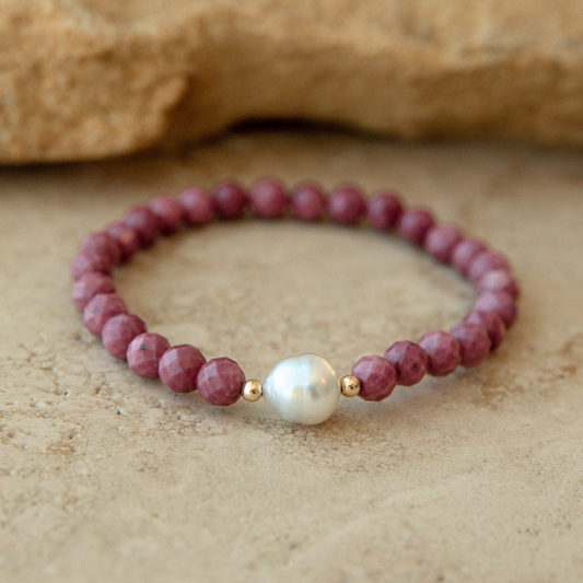 Faceted rhodonite beaded bracelet with an Australian South Sea circle pearl on a beige stone background