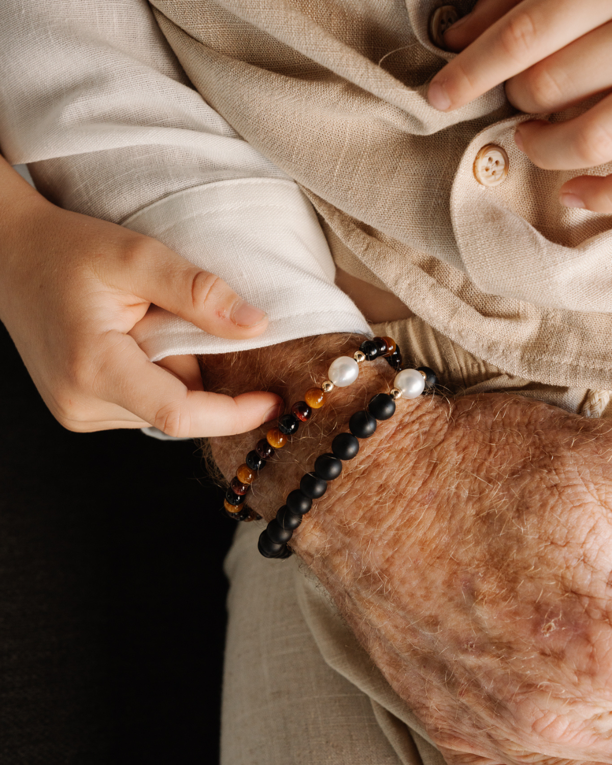 Person wearing a beige shirt and their Tigers Eye & Pearl Bracelet stacked with an Onyx & Pearl Bracelet.