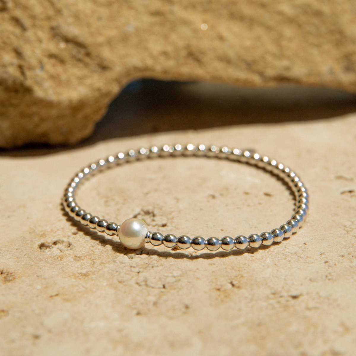 Silver beaded bracelet on a sandy surface with a rock in the background
