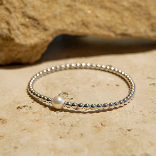 Silver beaded bracelet on a sandy surface with a rock in the background