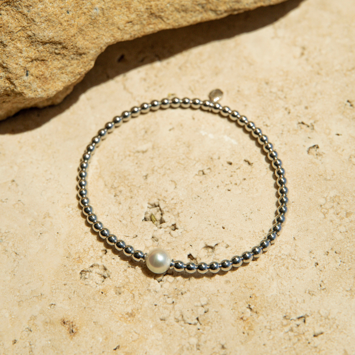 Silver beaded bracelet with a pearl on a beige stone surface