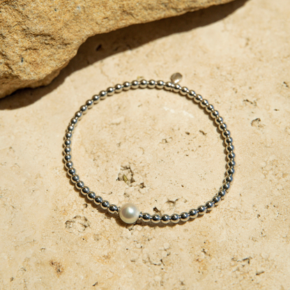 Silver beaded bracelet with a pearl on a beige stone surface