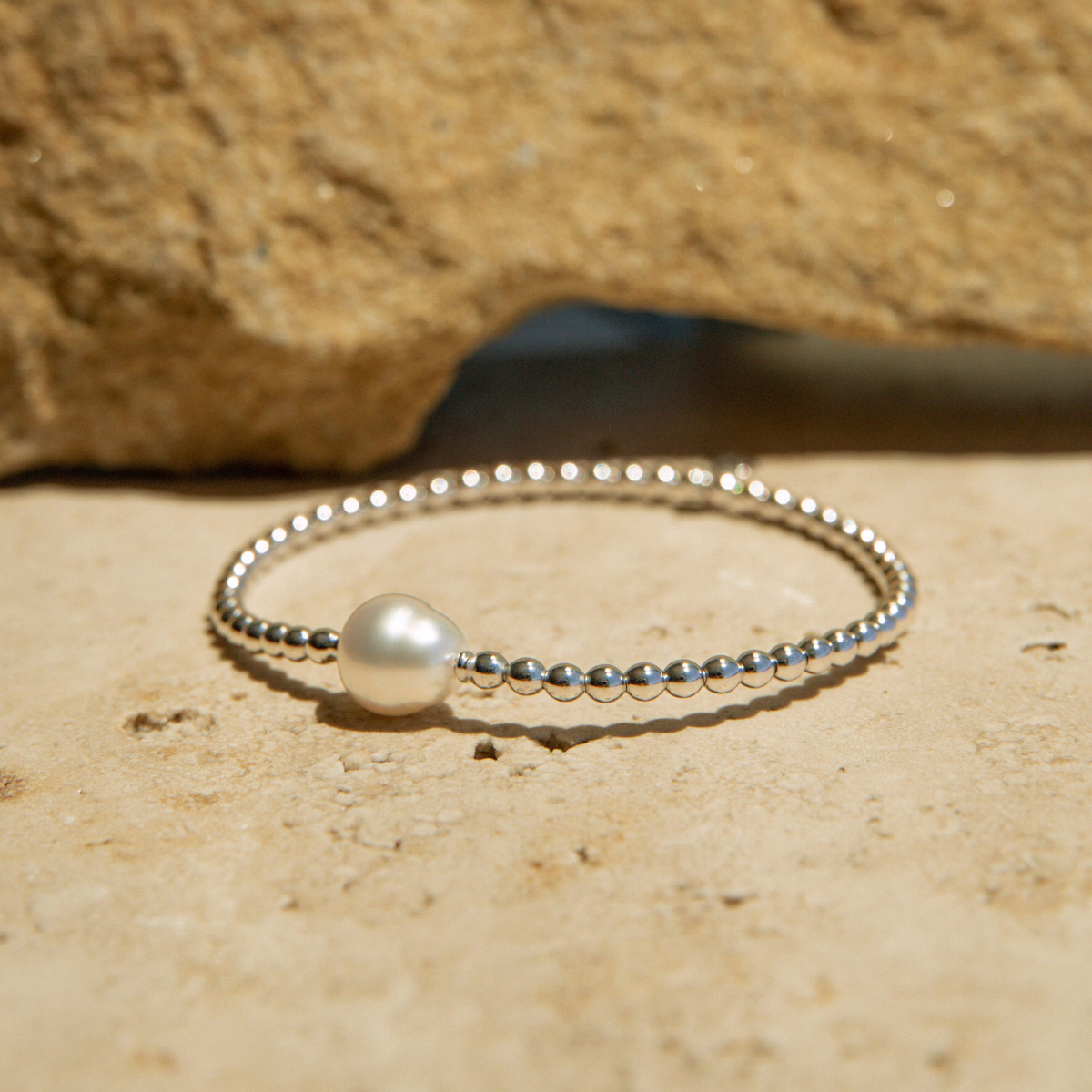 Silver bracelet with a pearl on a sandy surface