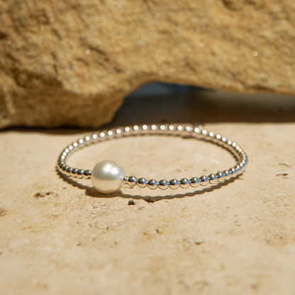 Silver bracelet with a pearl on a sandy surface