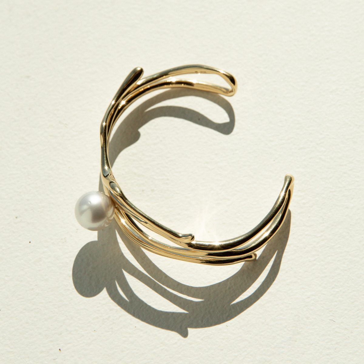 Gold cuff with a pearl on a beige background