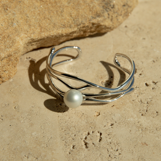 Silver bracelet with a pearl on a sandy surface