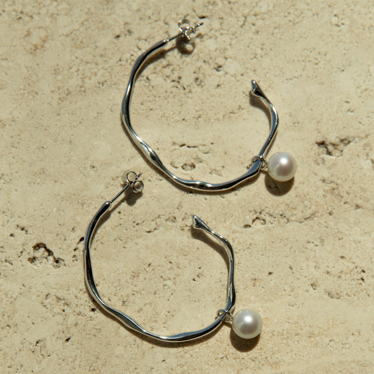 Silver hoop earrings with pearls on a beige surface