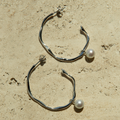 Silver hoop earrings with pearls on a beige surface