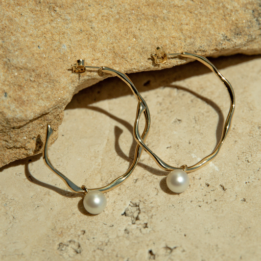 Gold hoop earrings with pearl drops on a stone surface