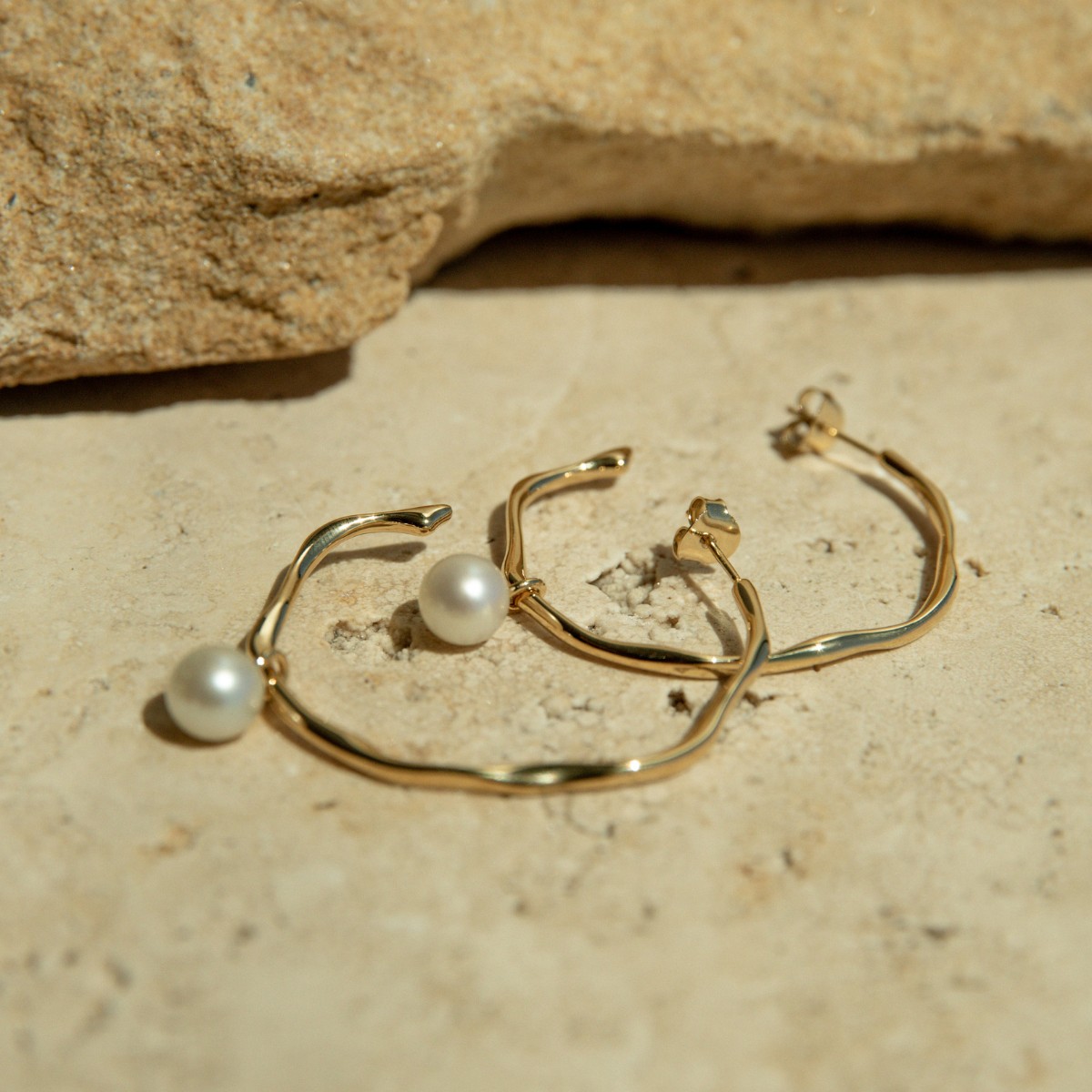 Gold hoop earrings with pearls on a beige stone surface