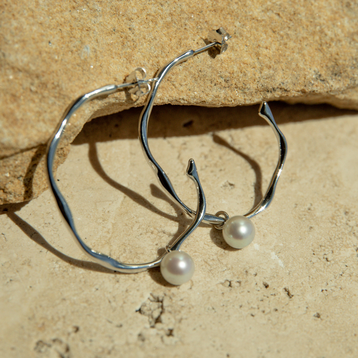 Silver hoop earrings with pearl drops on a stone surface