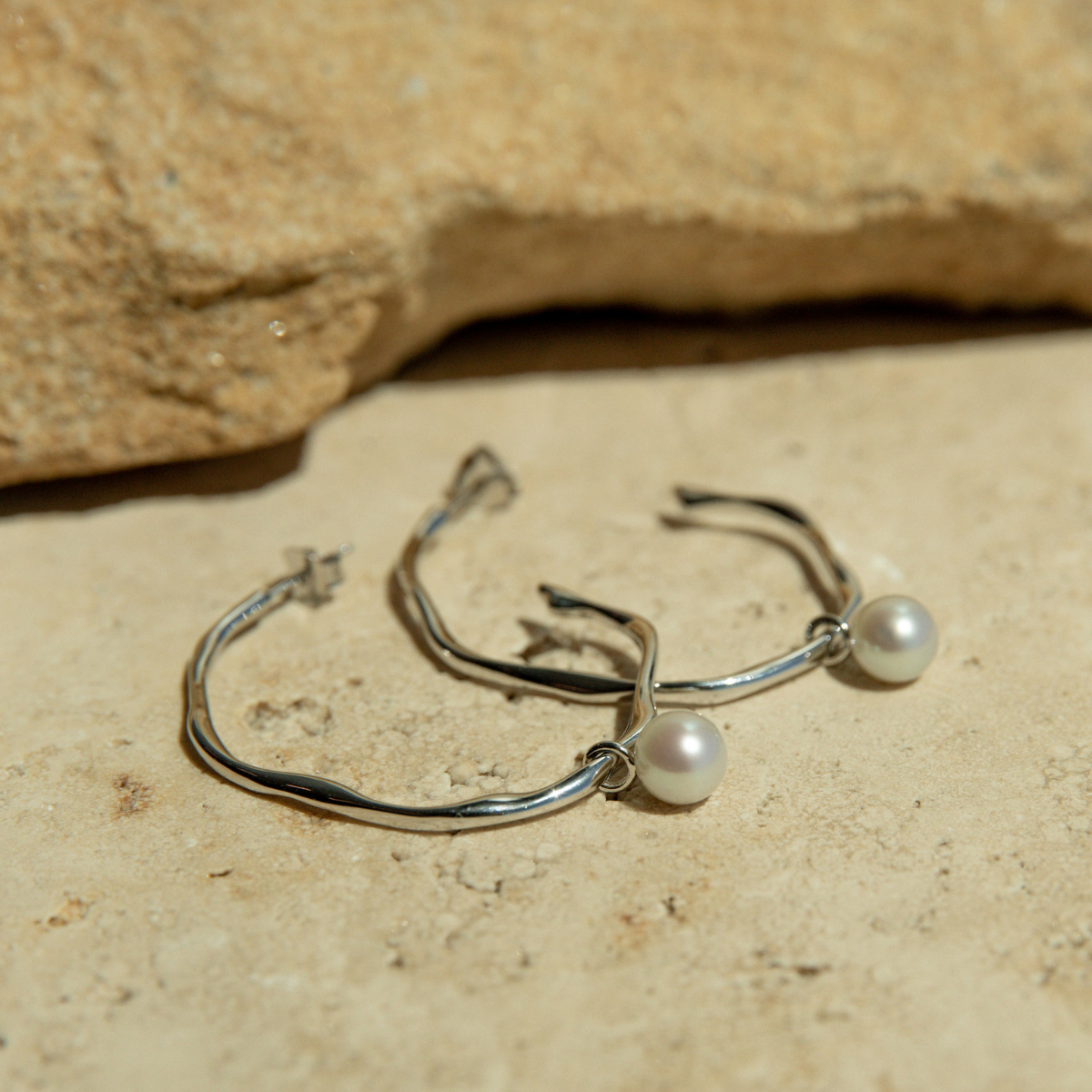 Silver hoop earrings with pearls on a stone surface