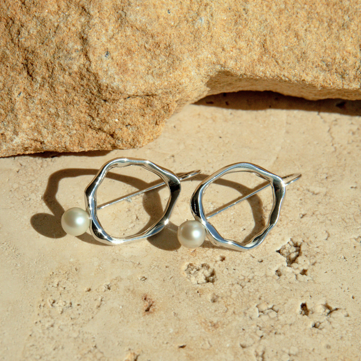 Silver earrings with pearl beads on a beige stone surface