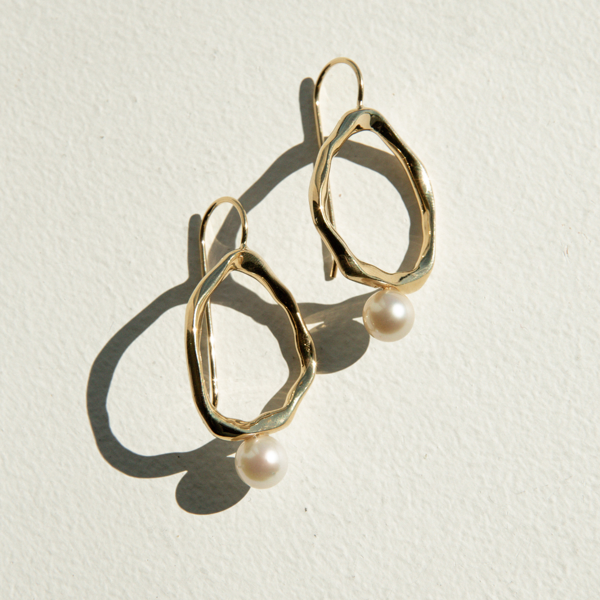Gold earrings with pearl drops on a light background