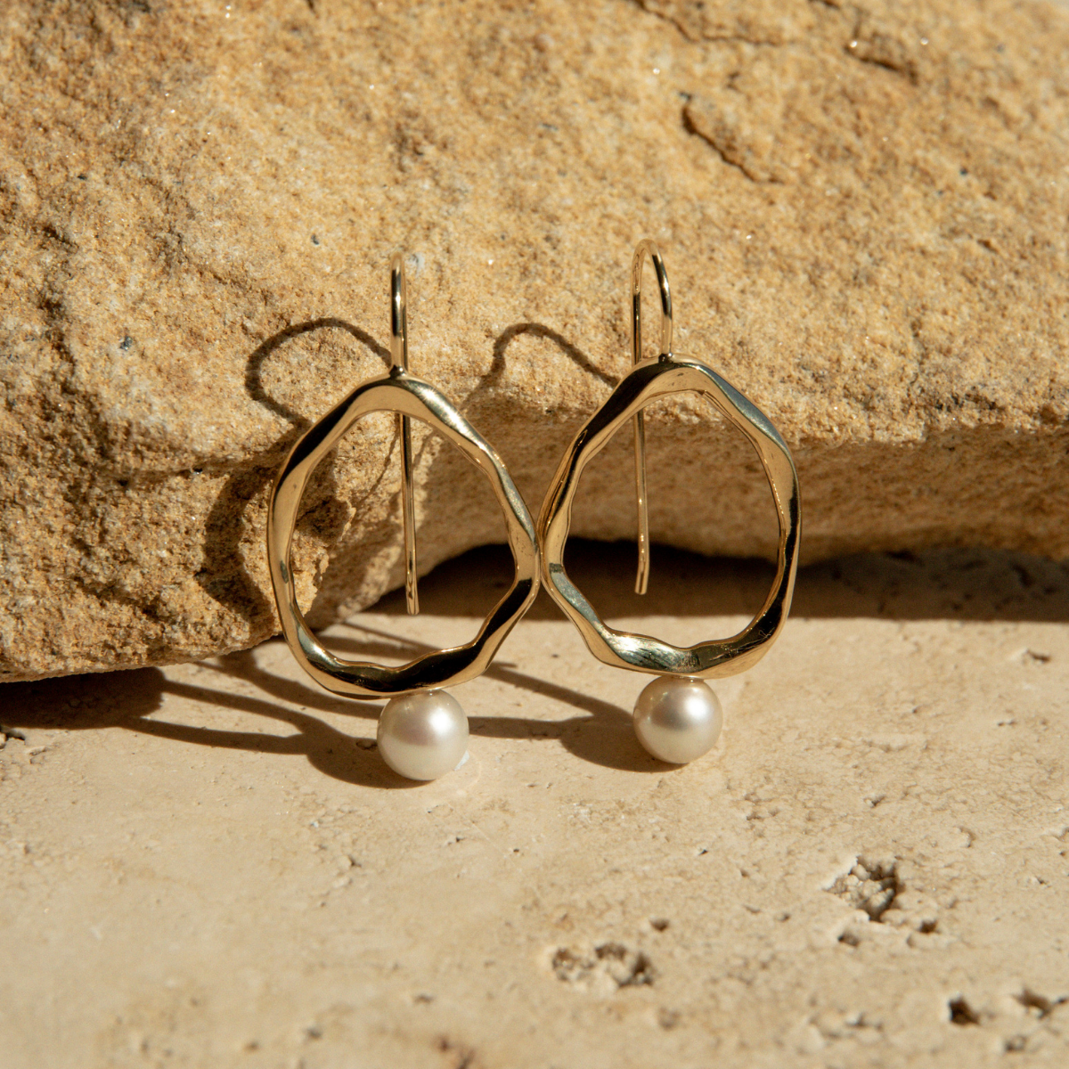 Gold earrings with pearl drops on a stone surface