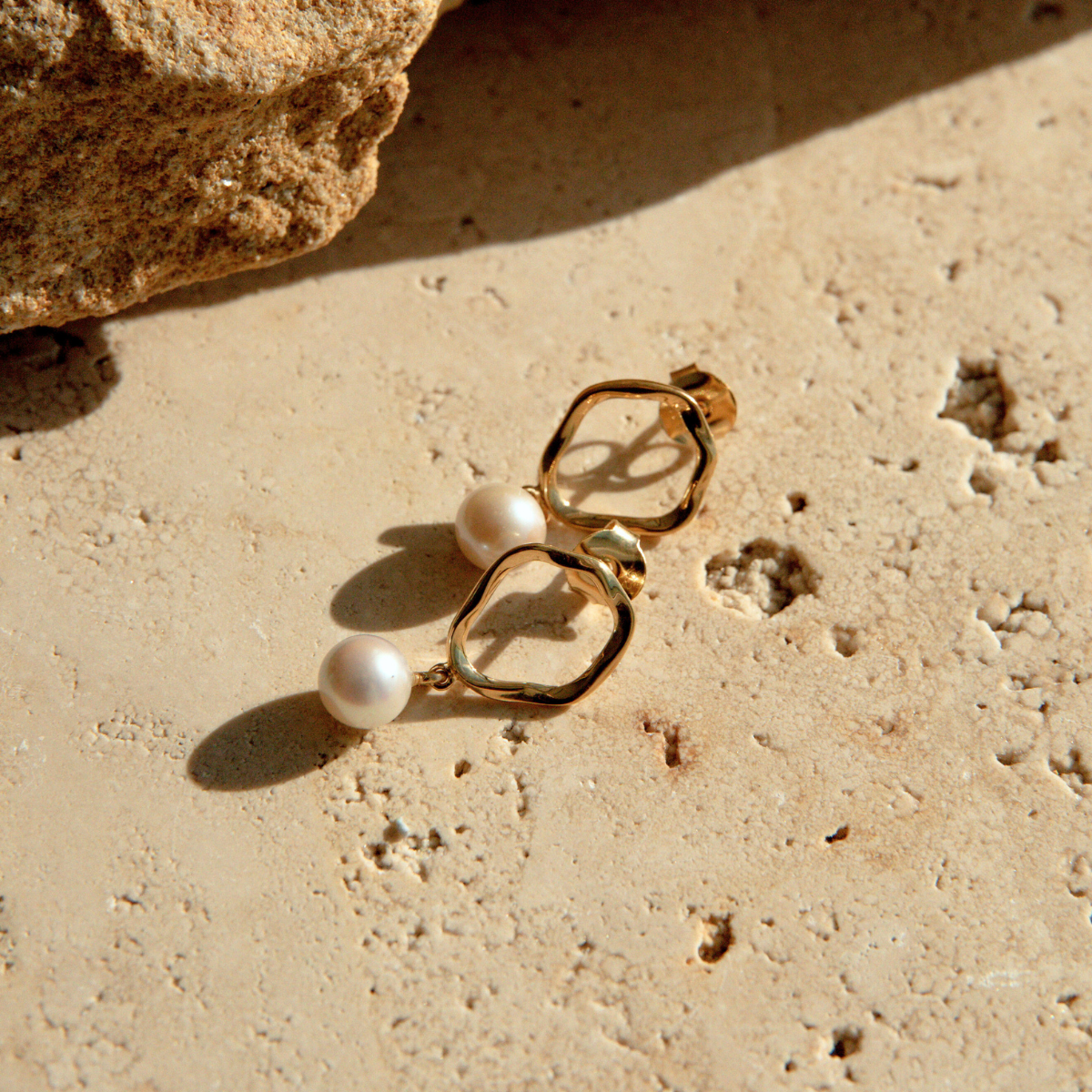 Gold earrings with pearls on a textured beige surface
