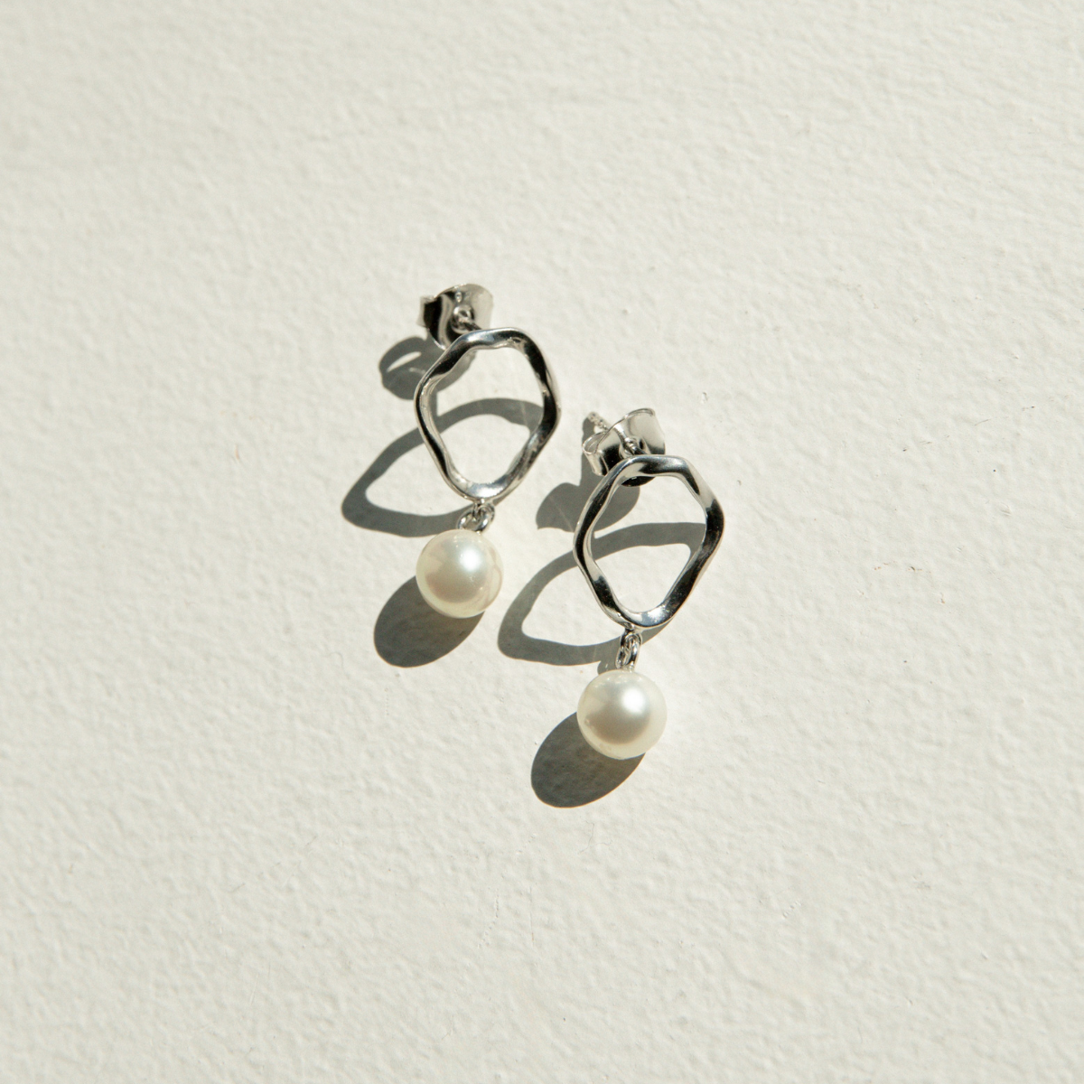 Silver earrings with pearl drops on a light beige background