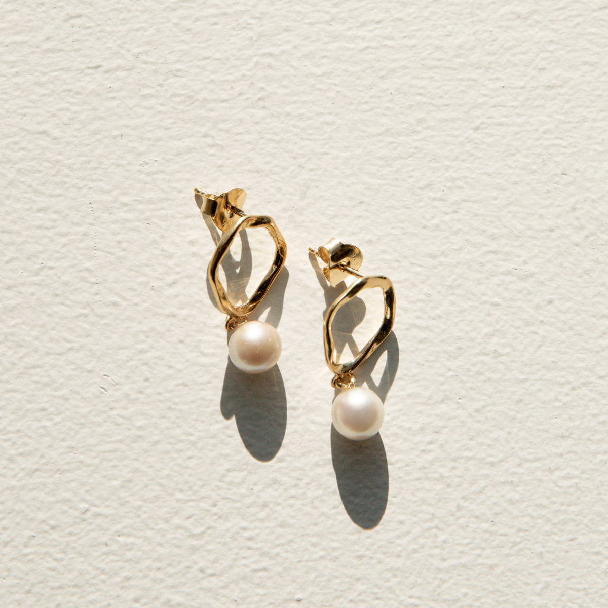 Gold earrings with pearls on a light gray background
