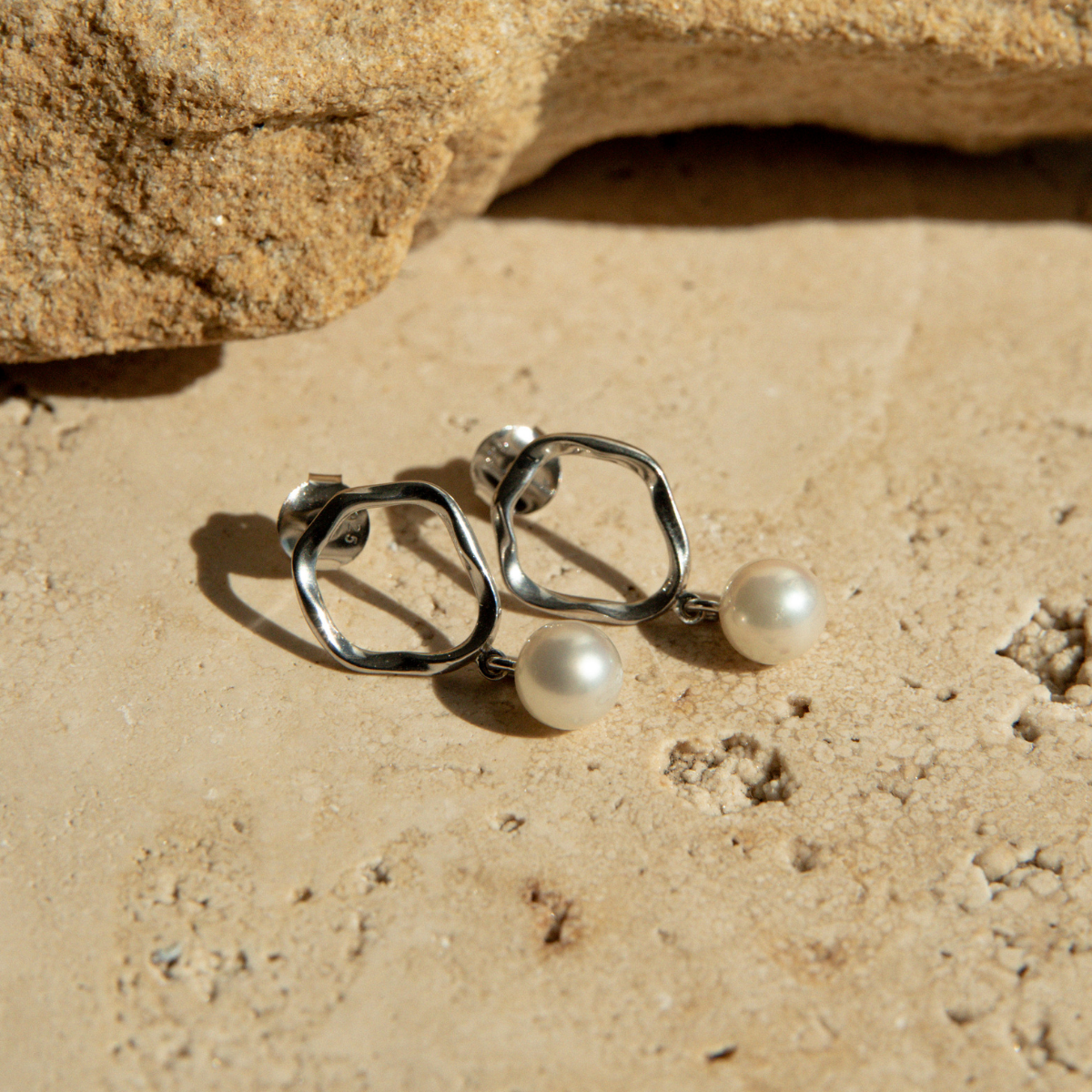 Silver hoop earrings with pearls on a sandy surface