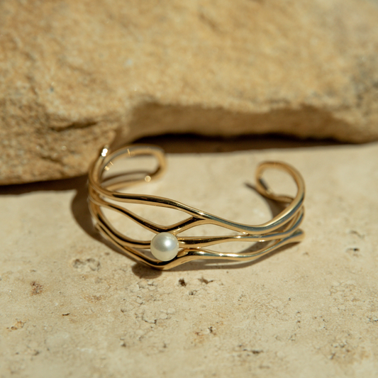 Gold bracelet with a pearl on a stone surface