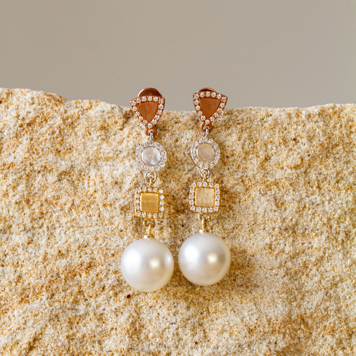 Pair of pearl earrings with gold and diamond accents on a textured beige surface