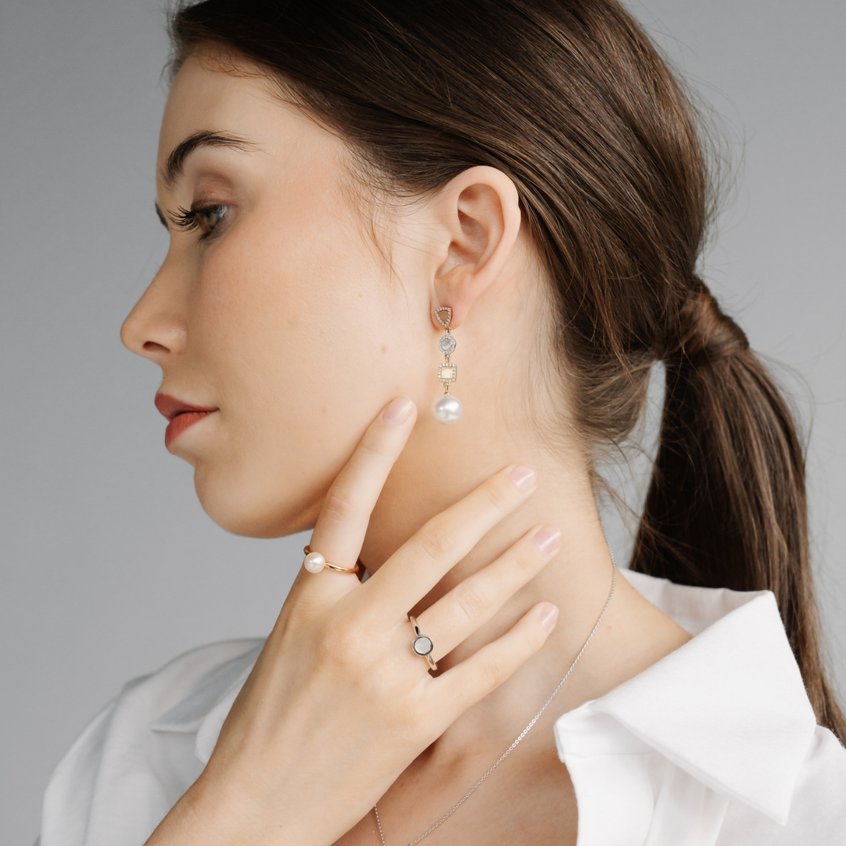 Woman wearing pearl earrings and a pearl ring, with a neutral background
