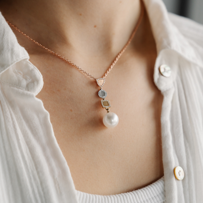 Necklace with a pearl pendant worn by a person in a white shirt.