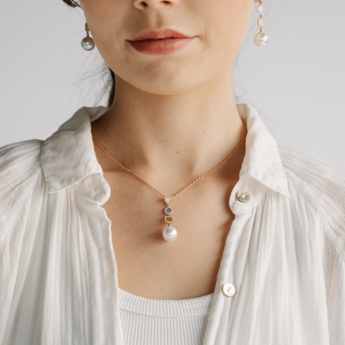 Person wearing a pearl necklace and earrings on a plain background