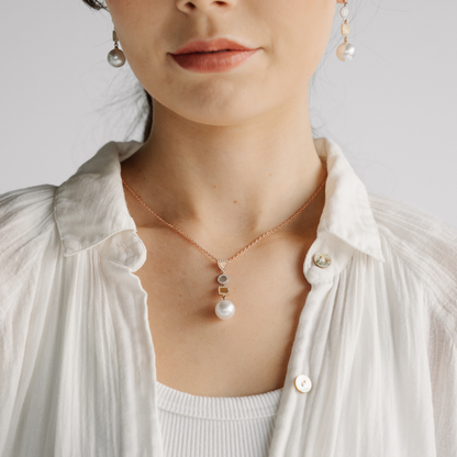 Person wearing a pearl necklace and earrings on a plain background