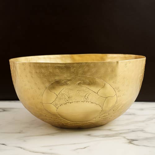 Gold bowl with engraved crab design on a marble surface