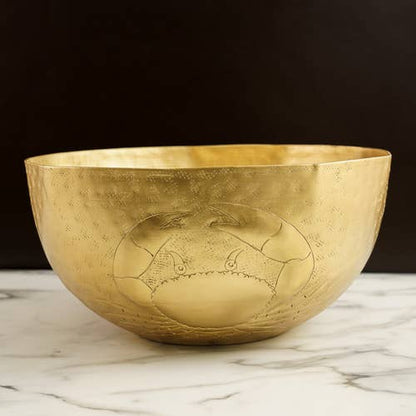 Gold bowl with engraved crab design on a marble surface