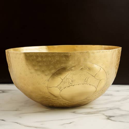 Gold bowl with engraved crab design on a marble surface